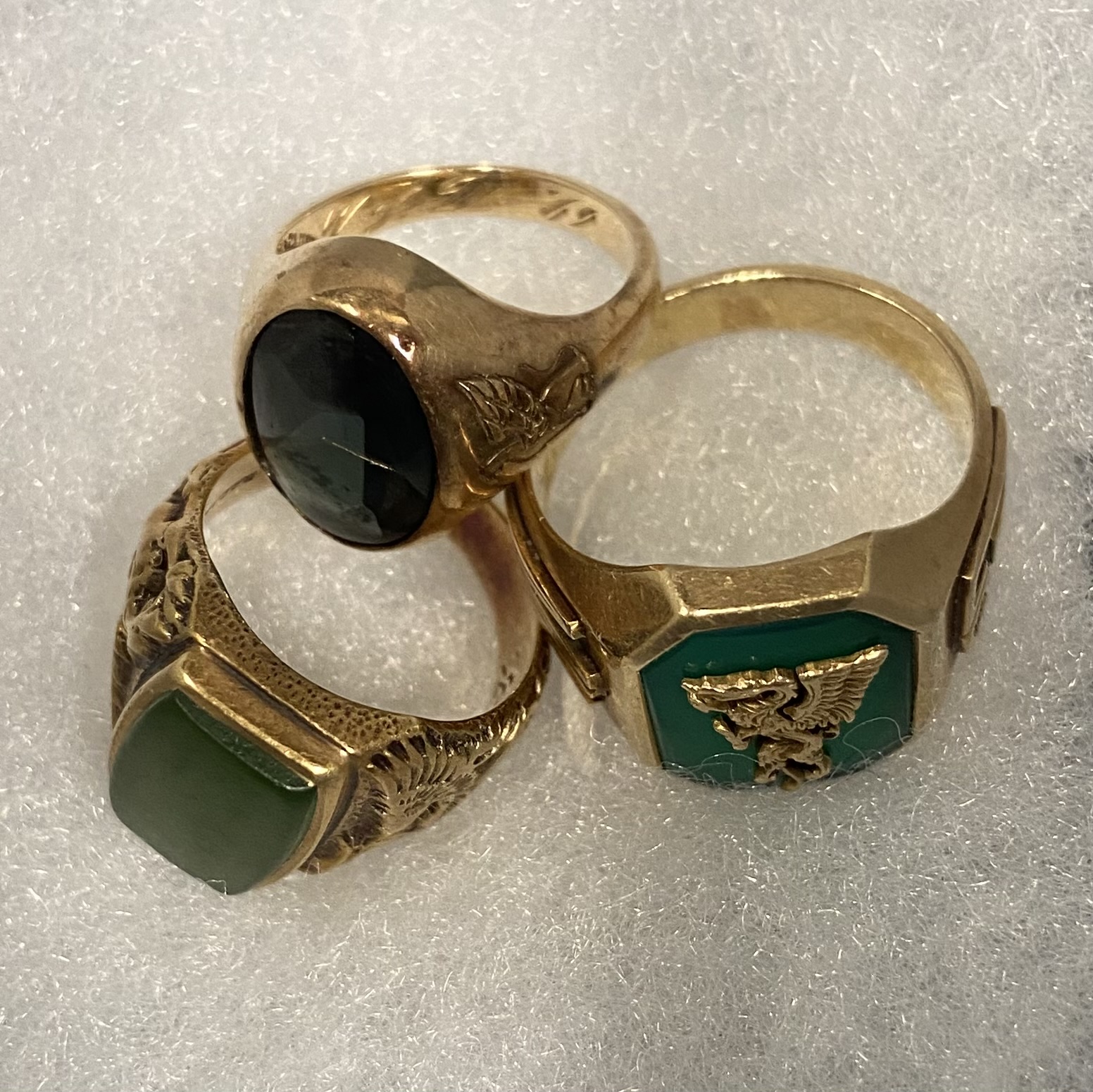 Three gold rings with green stones of different shapes. 