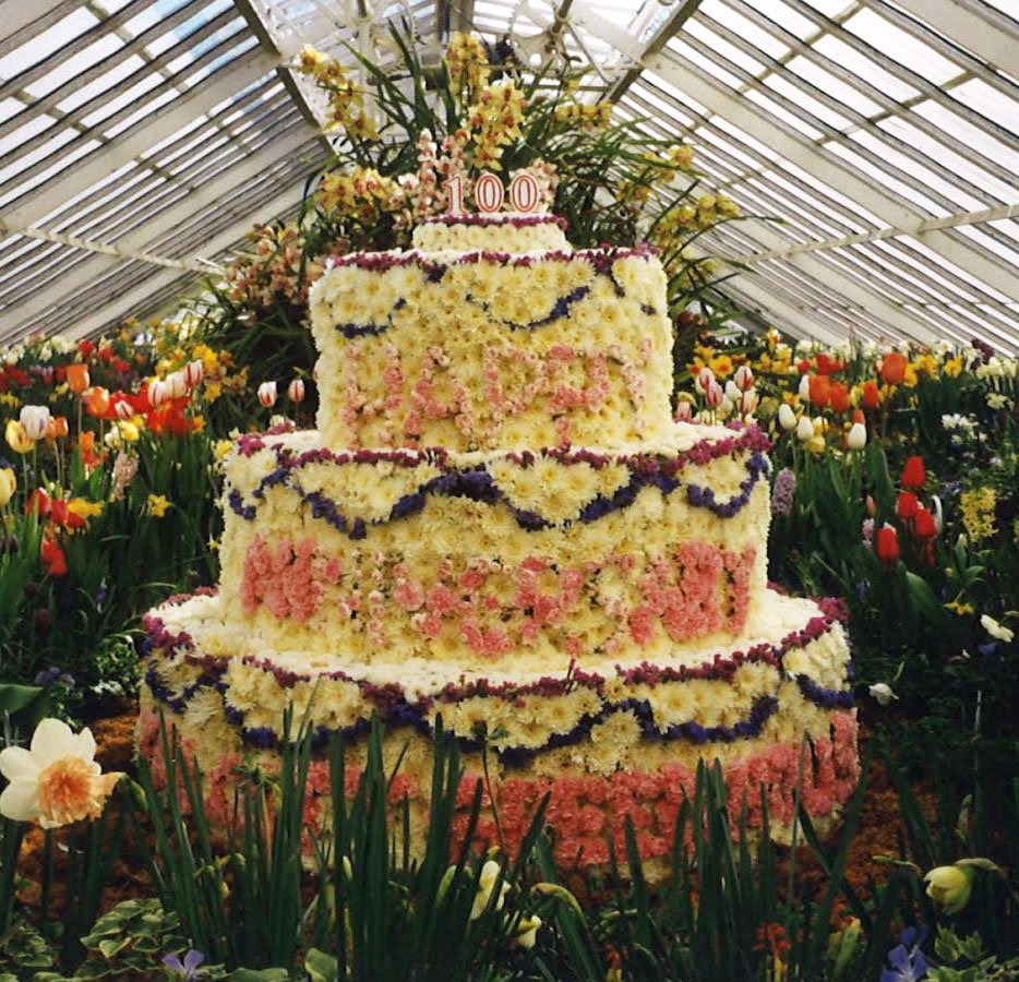 A colorful photo of a birthday cake made of flowers on display in a greenhouse.