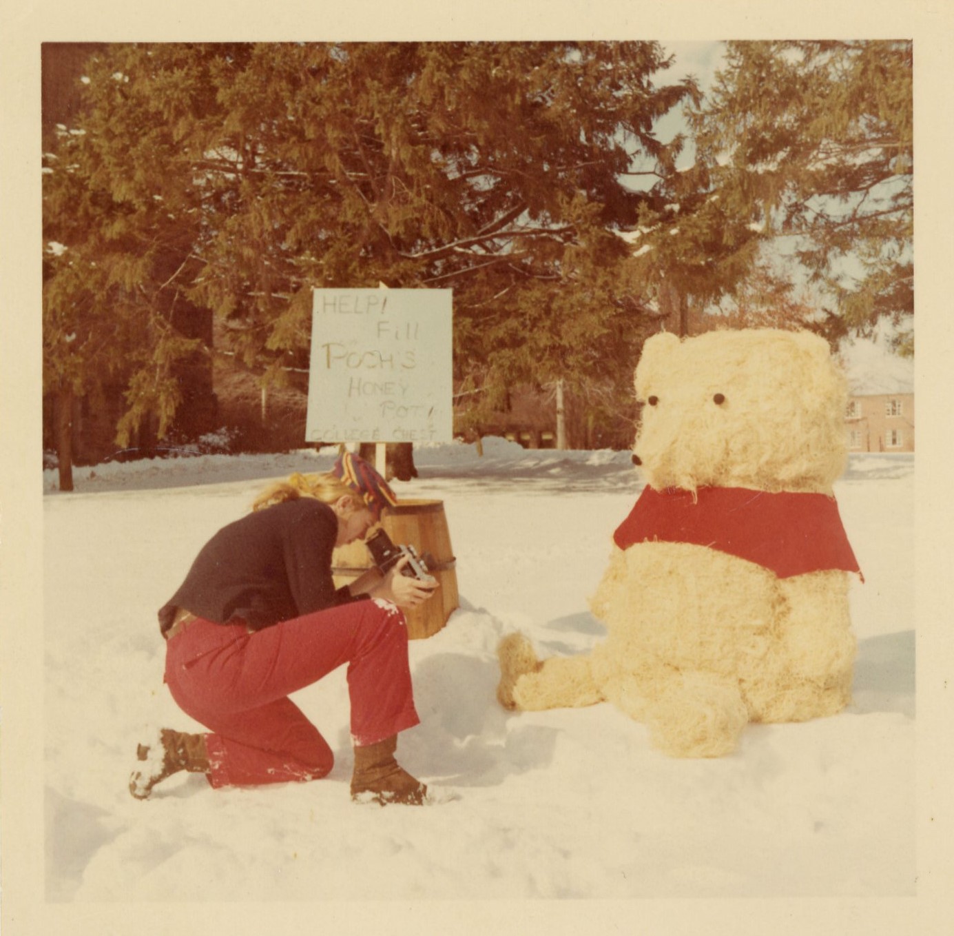 A student kneels in the snow to take a photo of a snow sculpture of Winnie the Pooh