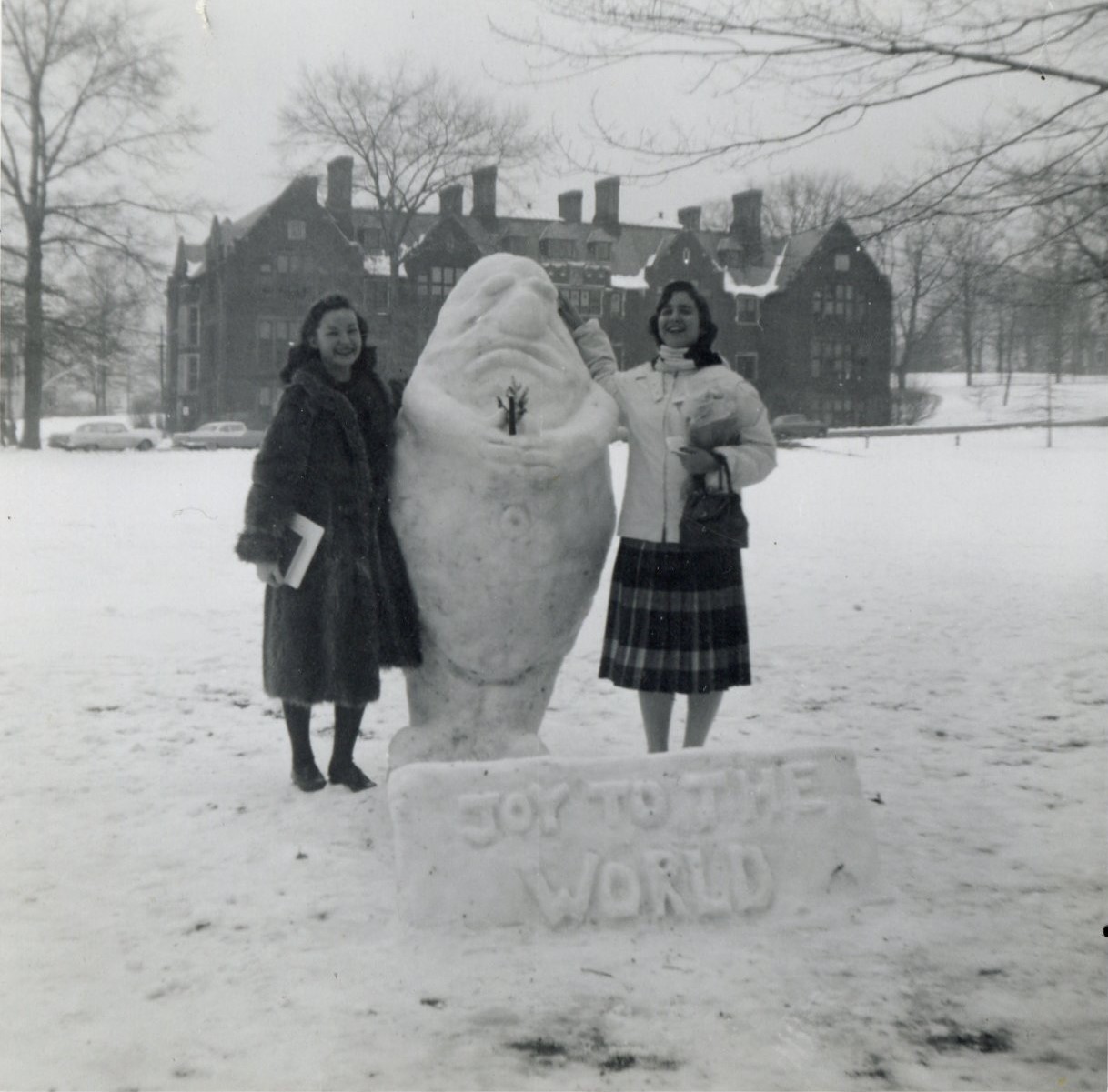 Students stand with a snow sculpture on Skinner Green.  A sign carved in the snow reads Joy to the Wolrd