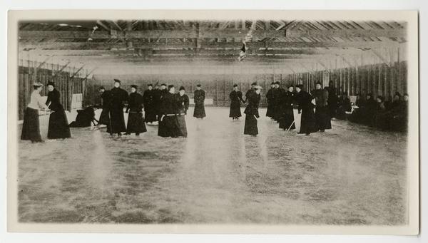 MHC students dressed in long dark dresses skate in an indoor skating rink in the later 1800s.