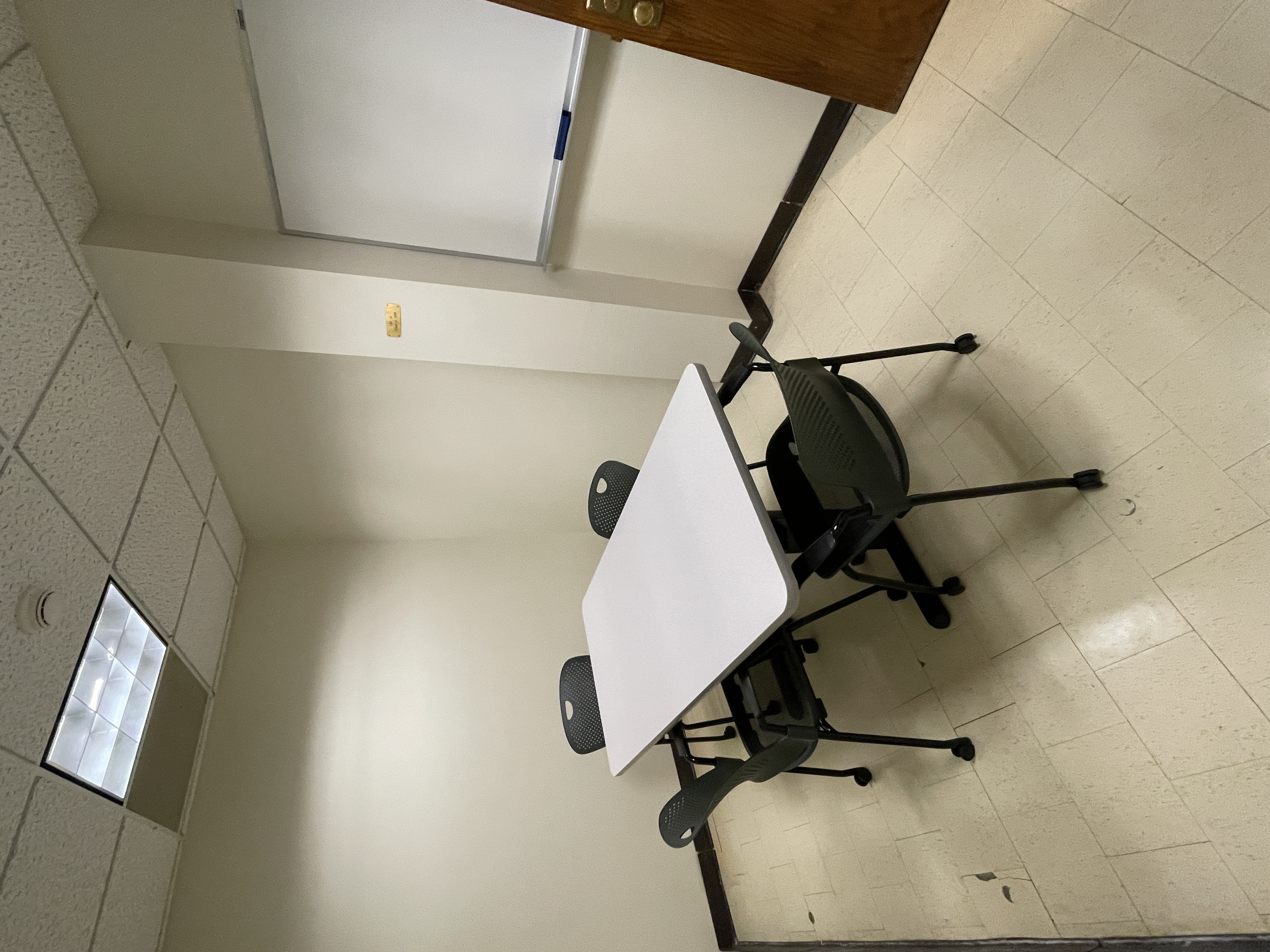 image shows table and 4 chairs, white board on wall