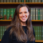 image show Krista in a black sweater, standing in front of green books on a self